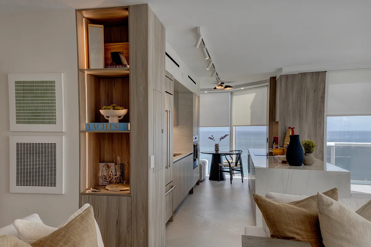 Great room looking past lit display shelving to the kitchen and the ocean